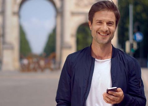 Bild eines M-Login Users, der sein Handy in der Hand hält und am Siegestor in München steht